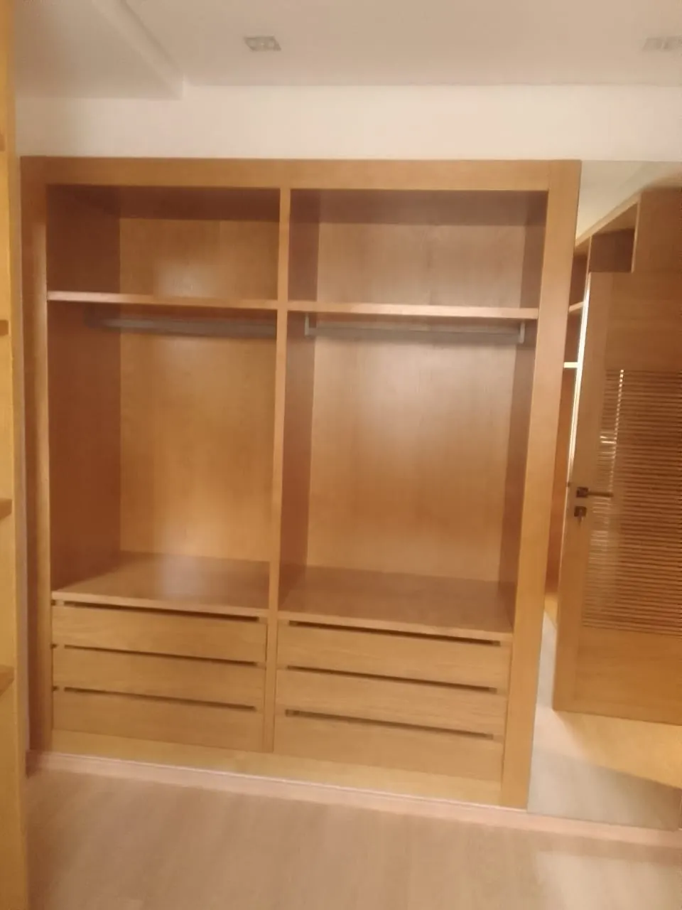 Armoire en bois clair ouverte : deux penderies au-dessus de quatre tiroirs.