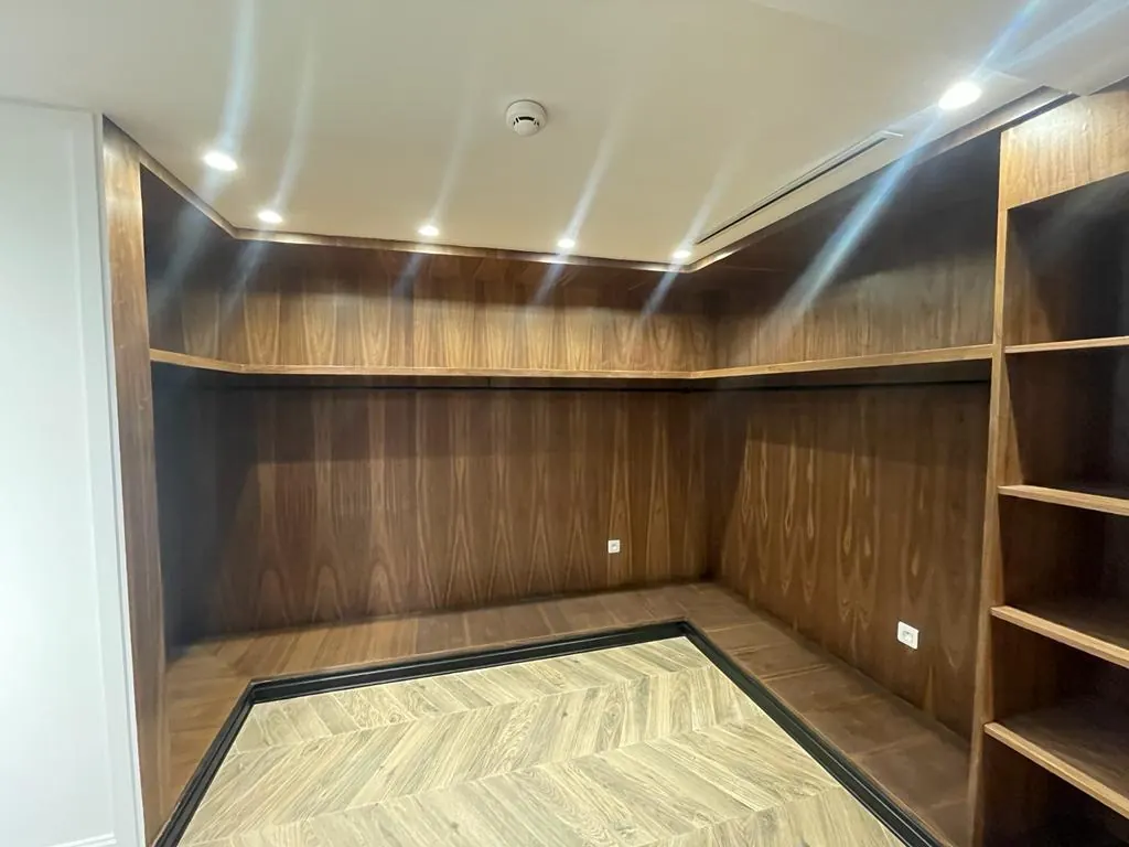 Dressing sur mesure en bois foncé veiné sur trois murs, penderie et étagères, parquet en point de Hongrie clair au sol.