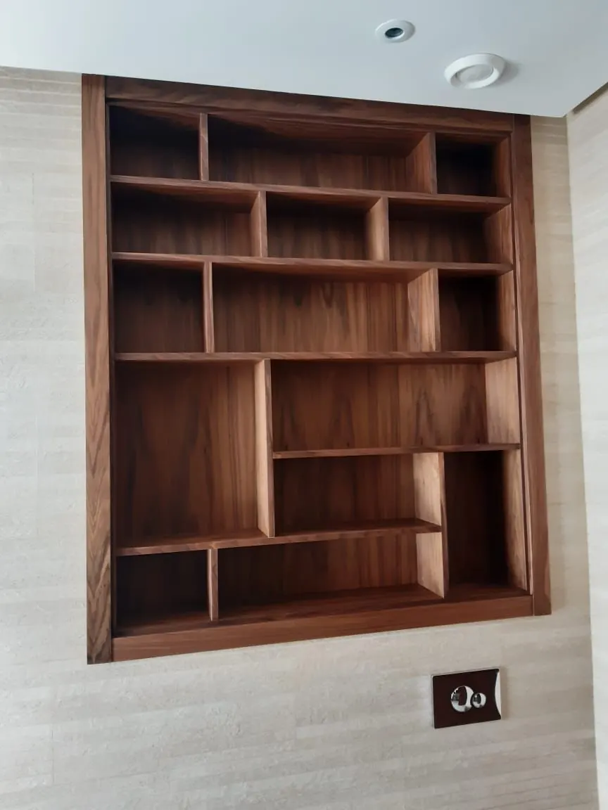 Bibliothèque encastrée en bois foncé, cases de tailles variées dans une niche murale.