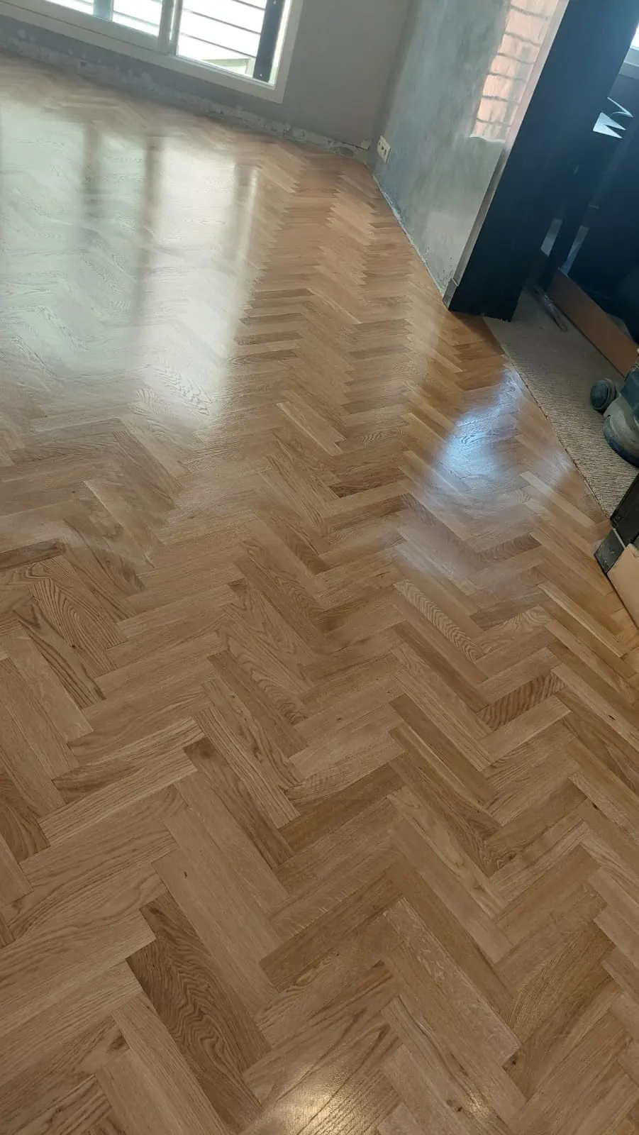 Parquet à bâtons rompus en bois clair vitrifié, lumière d’une fenêtre en reflet sur les lames.