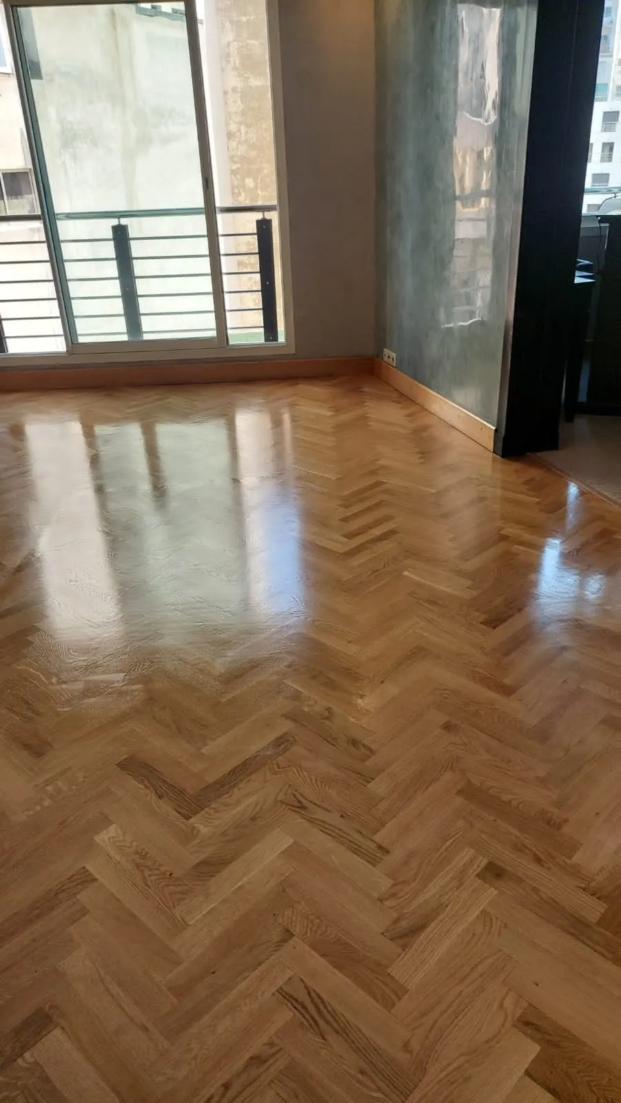 Parquet à bâtons rompus en bois clair vitrifié brillant, reflets d’une porte-fenêtre ouverte sur un balcon.