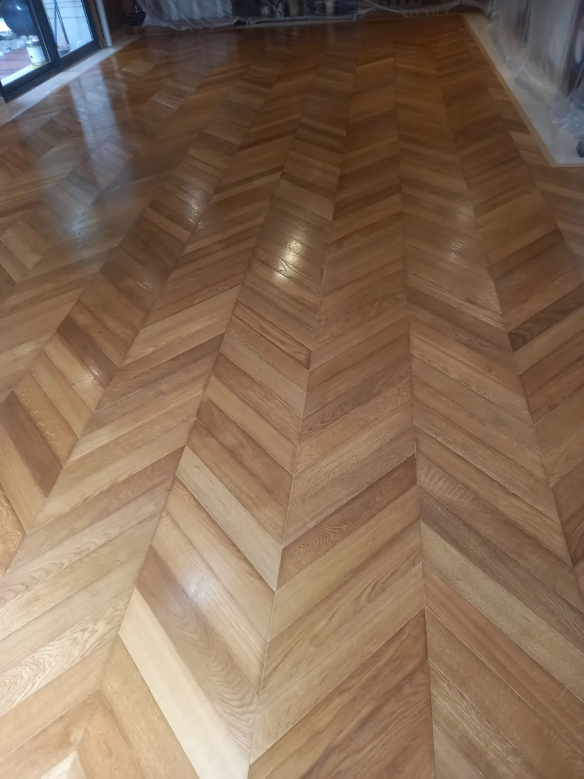 Parquet chevron, ou point de Hongrie, en bois clair vitrifié vu en enfilade, pointes des lames alignées.