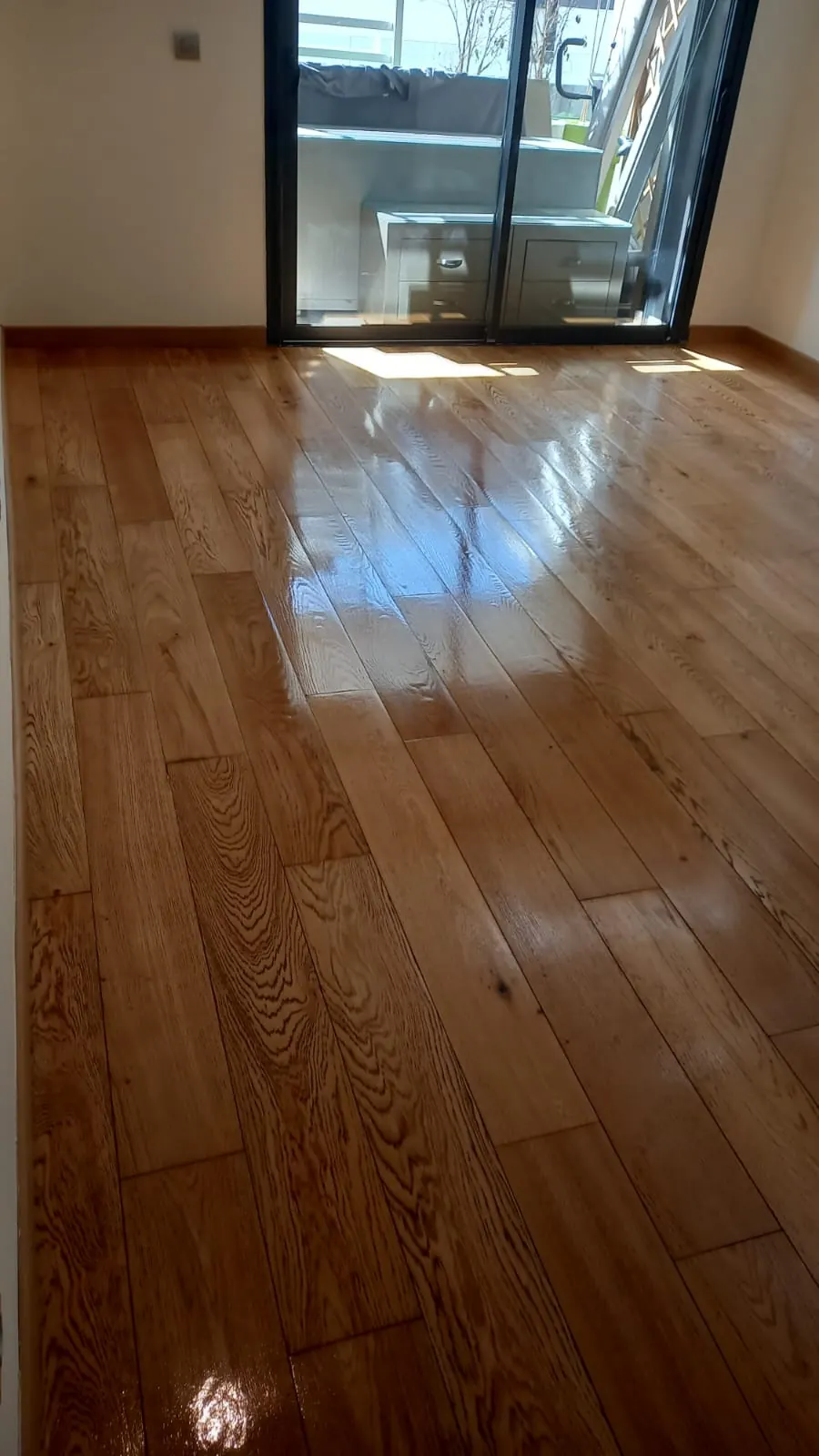 Parquet à lames en bois clair fraîchement vitrifié, au veinage marqué, soleil d’une baie vitrée sur le sol.