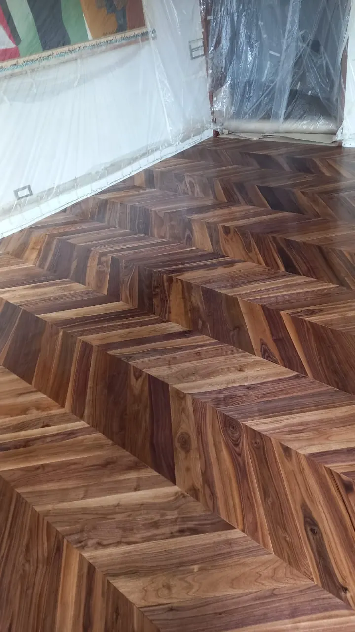 Parquet en point de Hongrie en bois brun veiné juste vitrifié, murs encore protégés par des bâches en plastique.