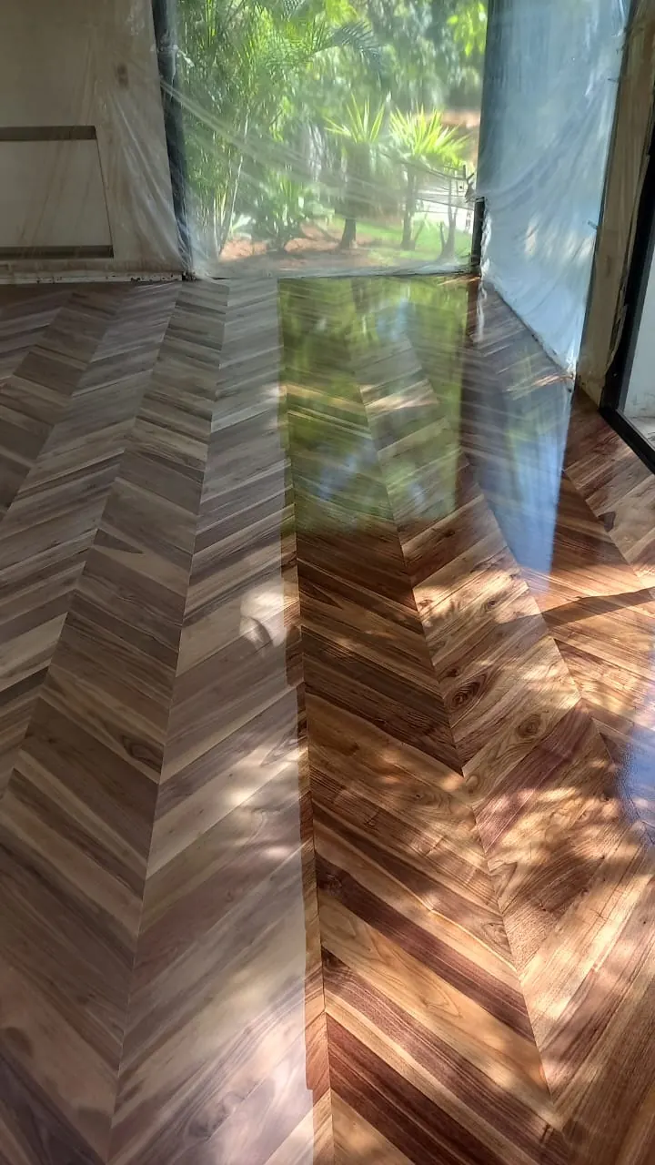Parquet en point de Hongrie en bois brun vitrifié, reflet d’un jardin dans le vernis, fenêtres encore bâchées.