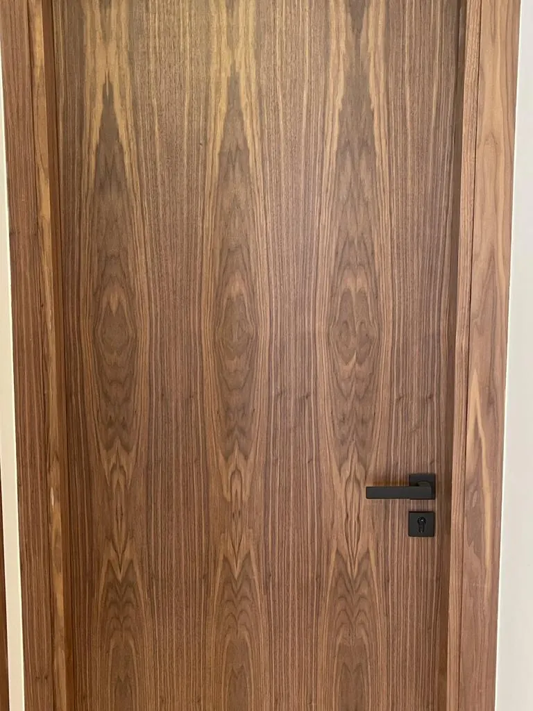 Porte en bois au veinage symétrique vue de près, poignée et serrure noires.