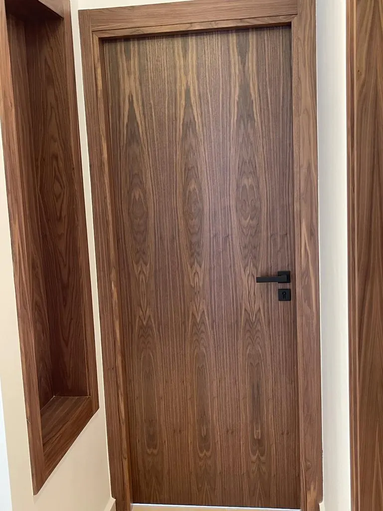 Porte intérieure en bois veiné foncé à poignée noire, chambranle en bois et niche murale à côté.