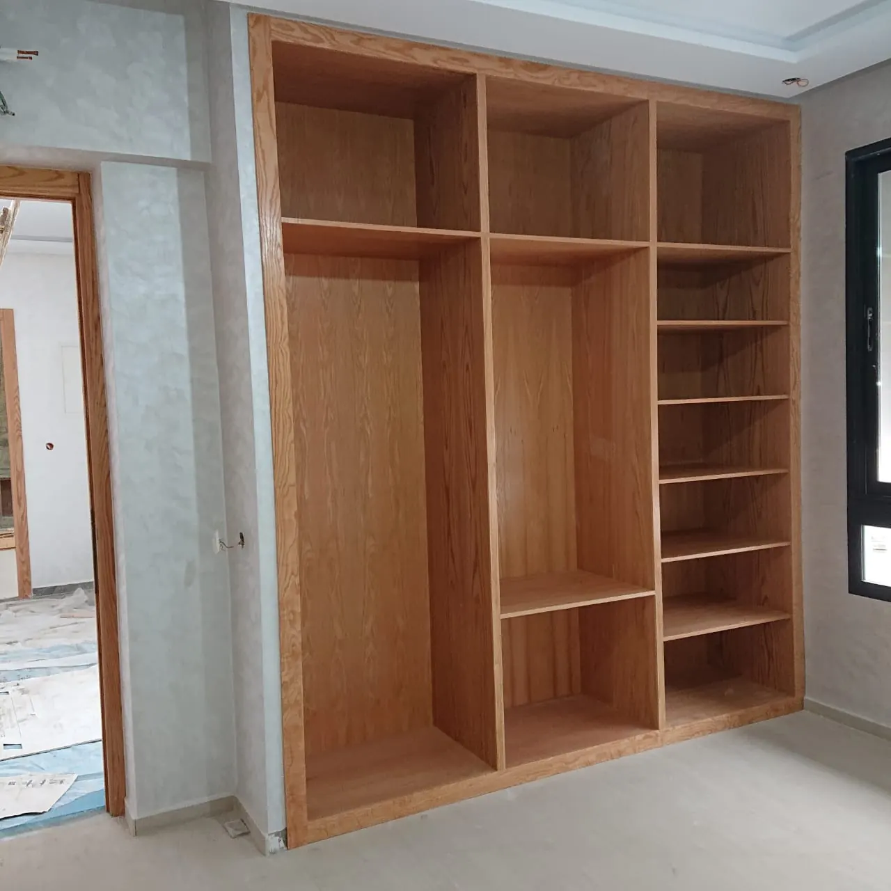 Rangement en bois clair en cours de pose dans une chambre : caissons, étagères et penderies encore vides.