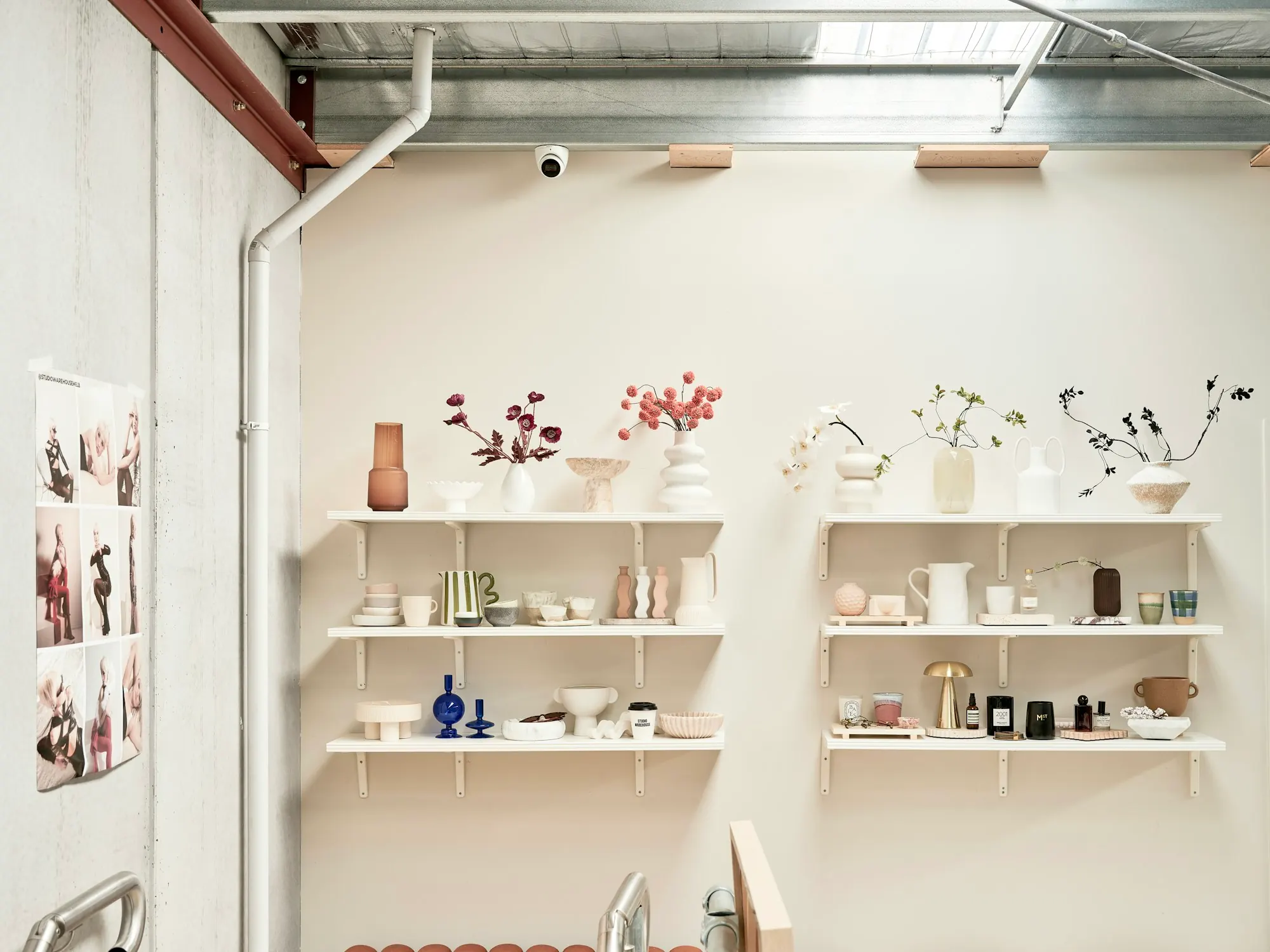 Agencement de boutique aux murs blancs : étagères garnies de vases et de céramiques, gaine apparente sous la verrière.