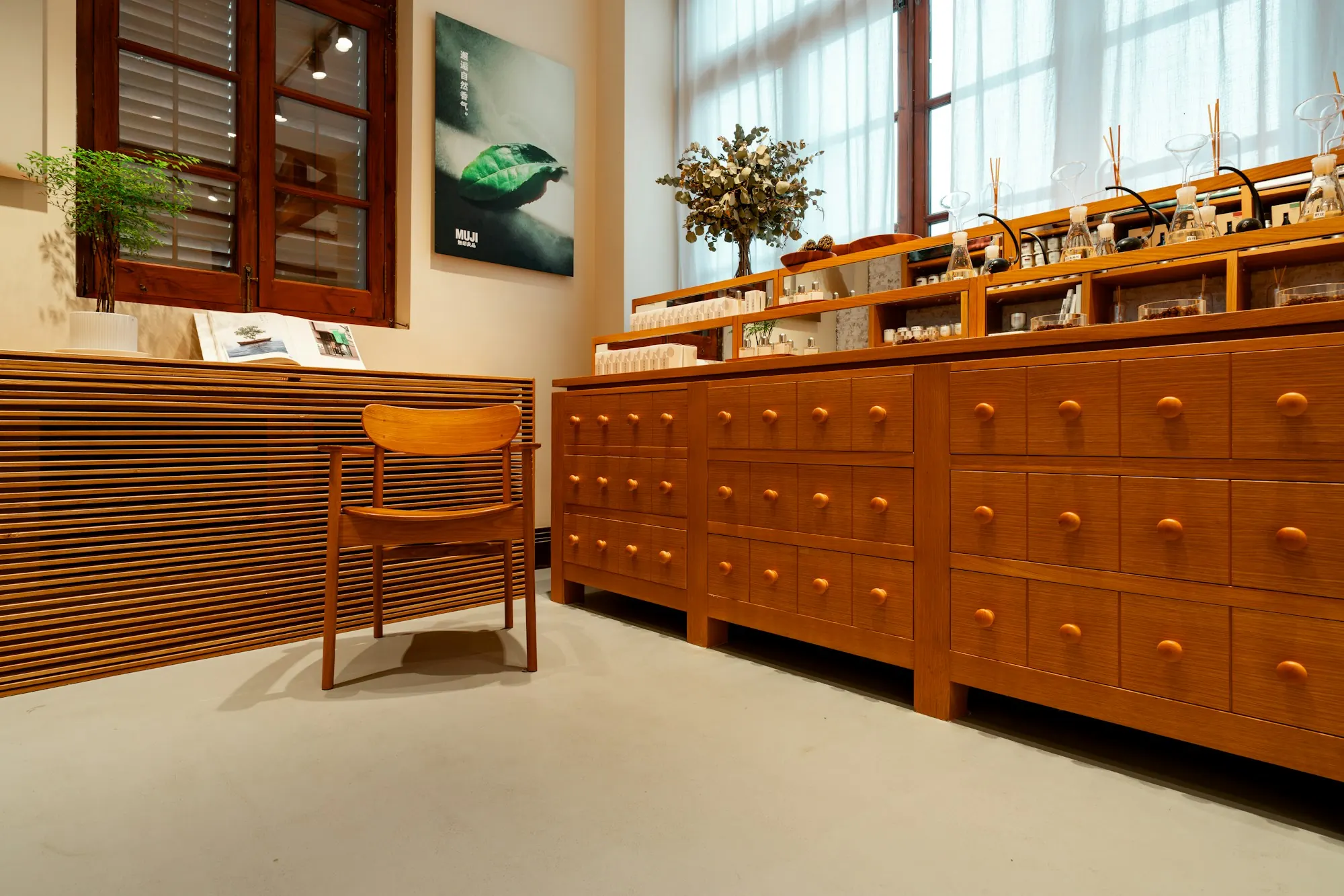 Agencement de boutique : grand meuble à tiroirs en bois teinté, meuble bas à lames horizontales, chaise en bois.