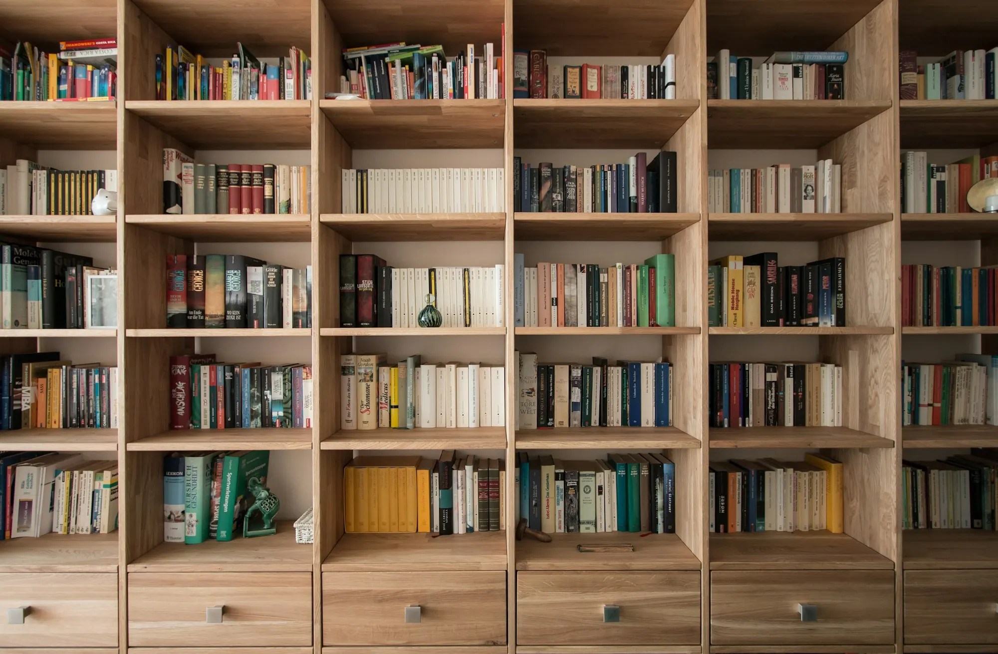 Bibliothèque en bois clair à cases régulières garnies de livres, tiroirs à boutons en partie basse.