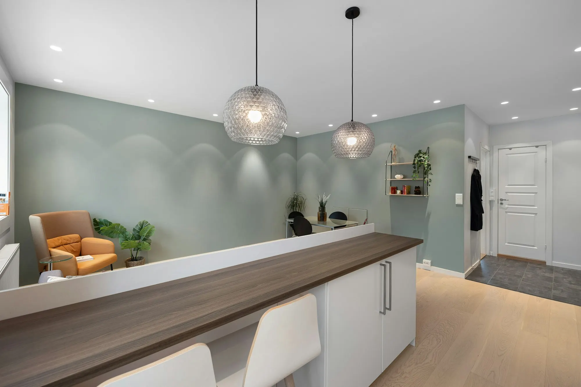 Comptoir d’accueil de cabinet : plateau en bois foncé sur caisson blanc, mur vert d’eau, suspensions en verre, parquet clair.