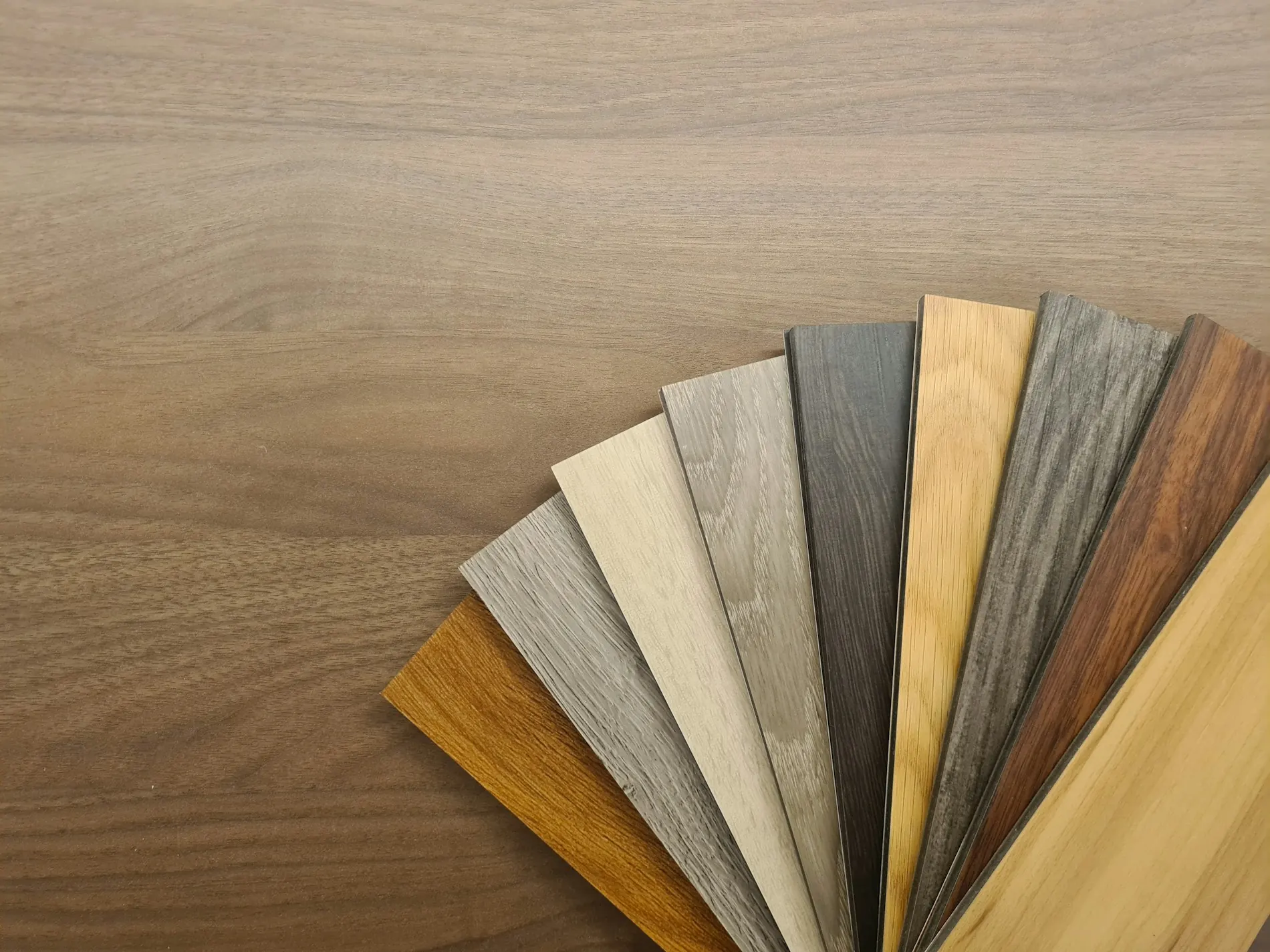 Éventail d’échantillons de lames d’aspect bois, du gris clair au brun, posé sur un plateau en bois.