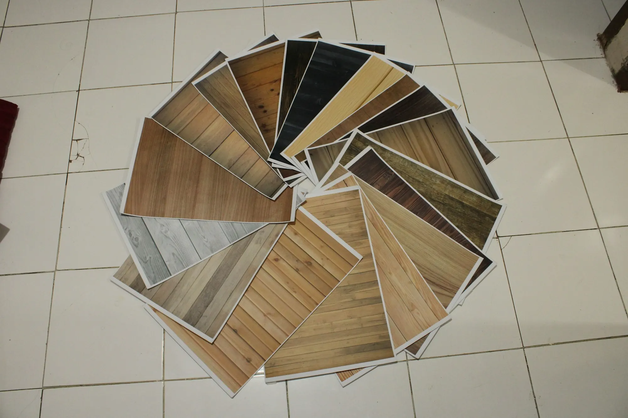 Échantillons de revêtement de sol d’aspect bois disposés en rosace sur un carrelage blanc.
