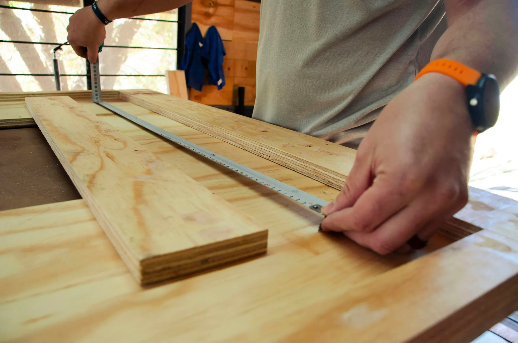 Mains traçant à la règle métallique sur des planches de contreplaqué posées sur un établi.