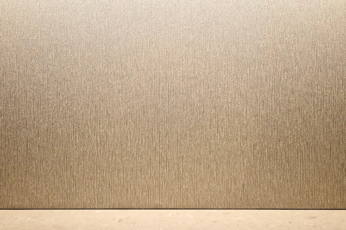 Mur revêtu d’un papier peint beige à texture verticale, vu de face.