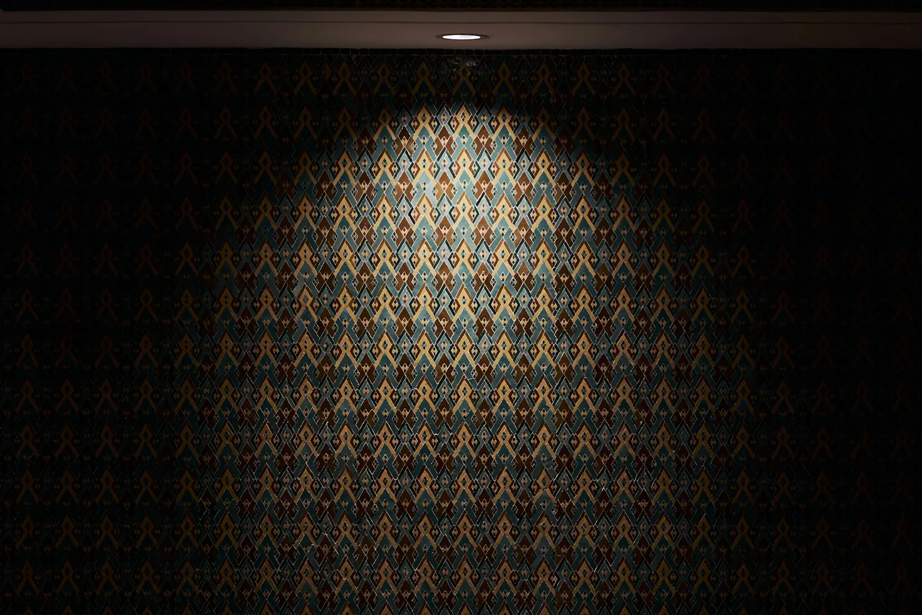 Papier peint à motif losangé sombre, éclairé de haut par un spot qui en fait ressortir le relief.