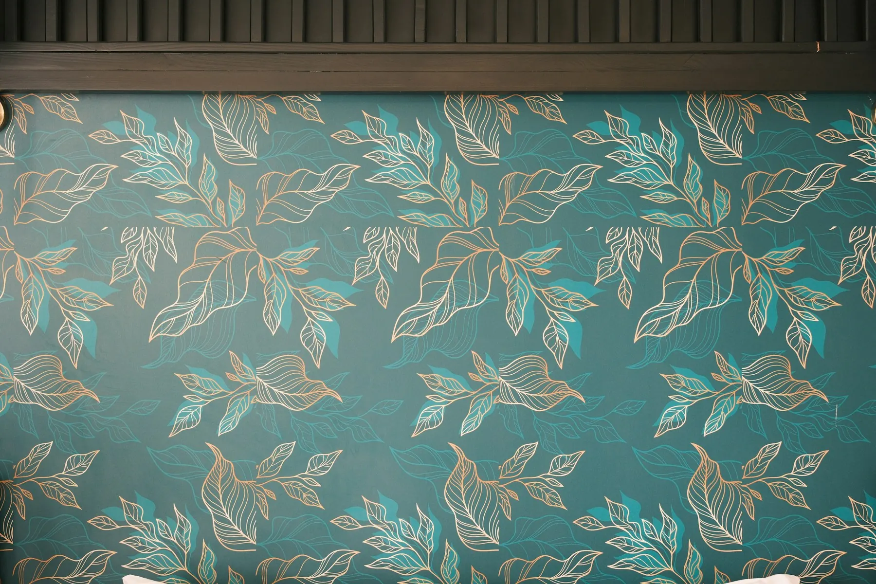 Papier peint bleu canard à feuillage dessiné en traits dorés, motif répété d’un lé à l’autre.