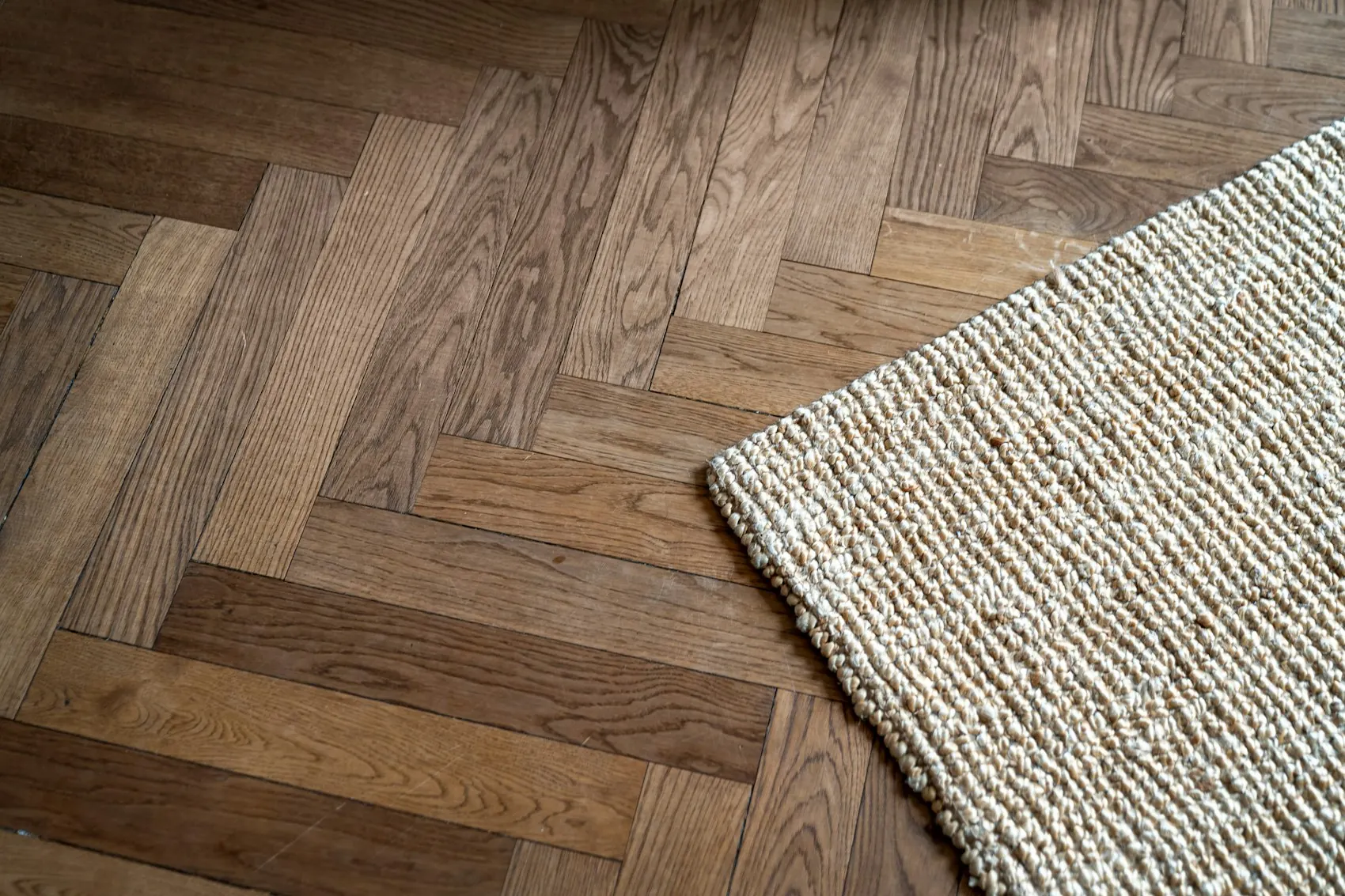Parquet à bâtons rompus en bois patiné vu de près, coin d’un tapis de jute.