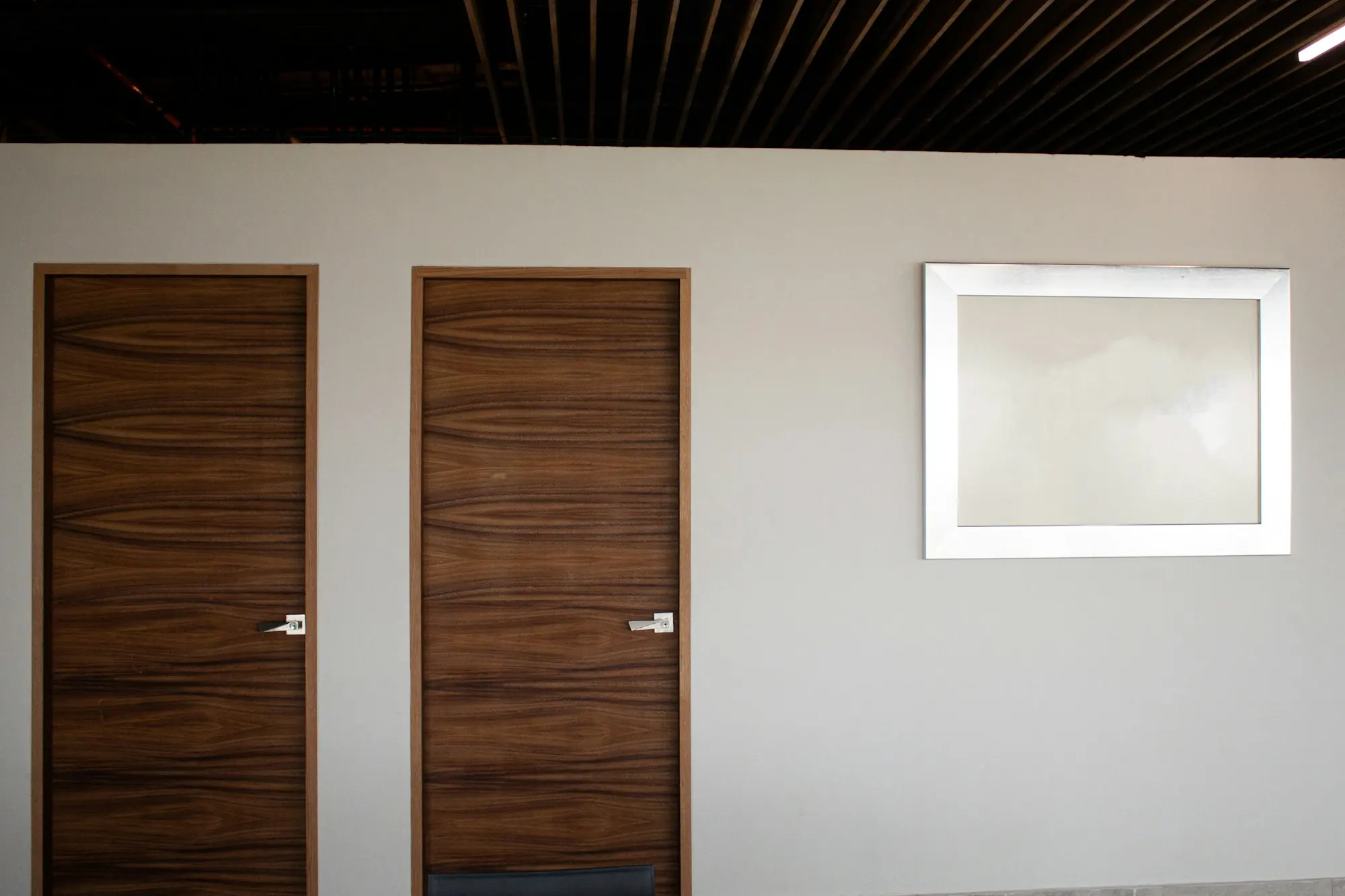 Deux portes en bois veiné sombre à poignées argentées dans un mur clair, cadre blanc à côté.