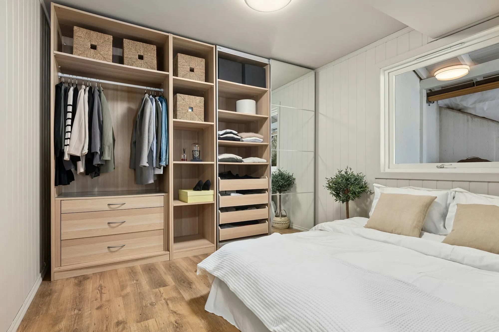 Rangement ouvert en bois clair dans une chambre : penderie, tiroirs et paniers, porte coulissante à miroir.