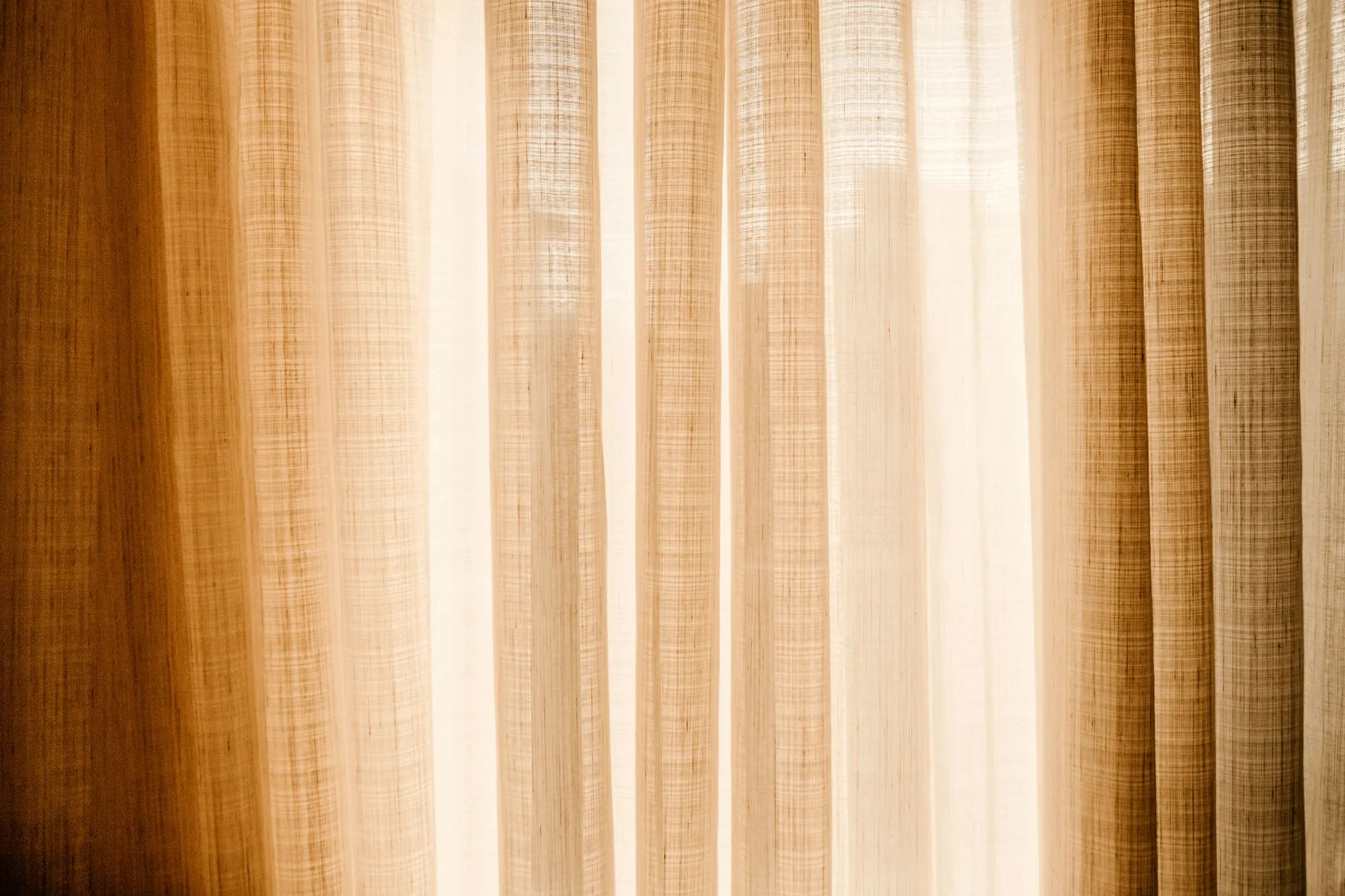 Rideau de lin à plis réguliers traversé par une lumière chaude, tissage visible.