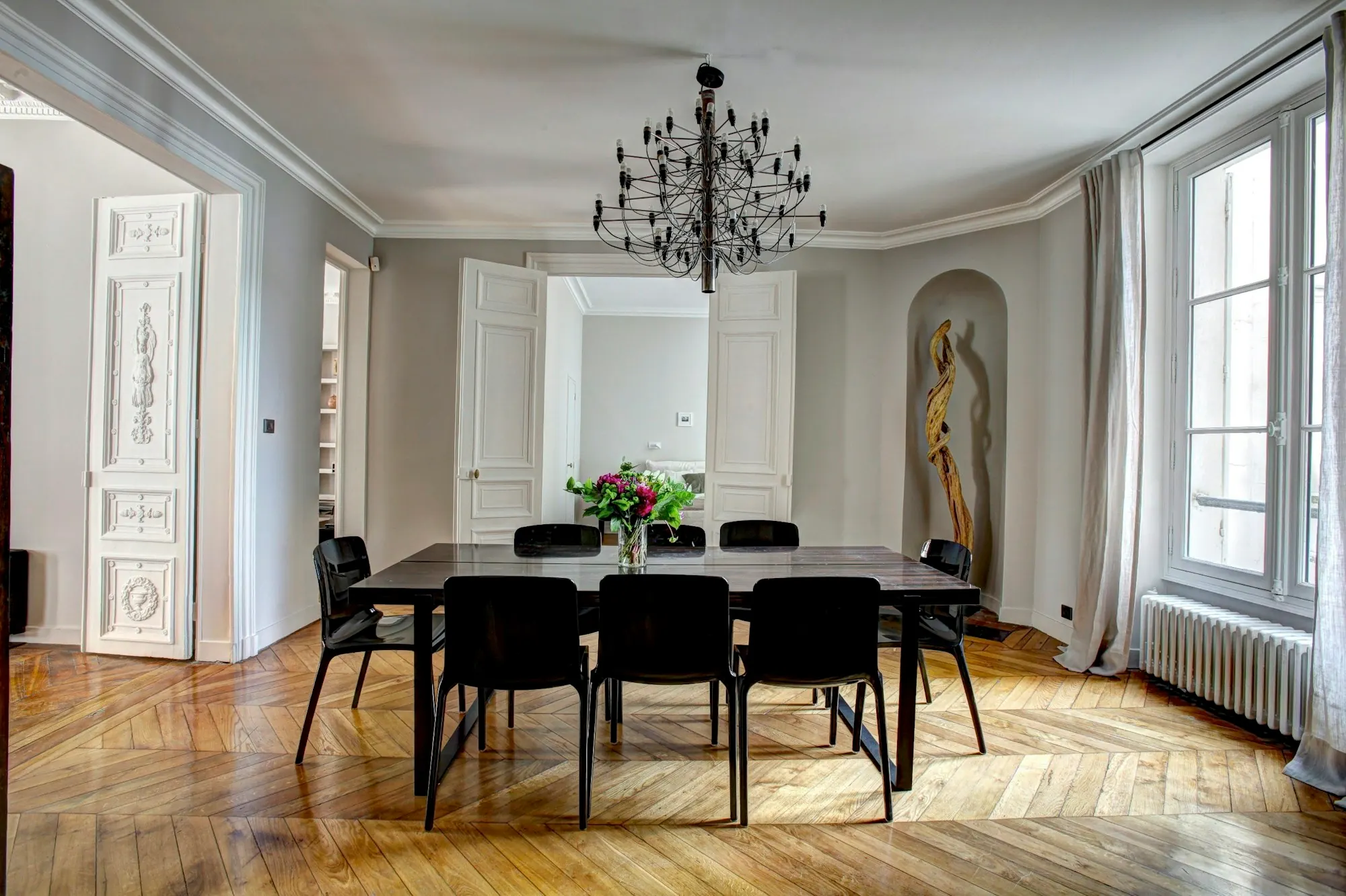 Salle à manger haussmannienne : parquet en point de Hongrie, table noire, lustre, portes à moulures et radiateur en fonte.