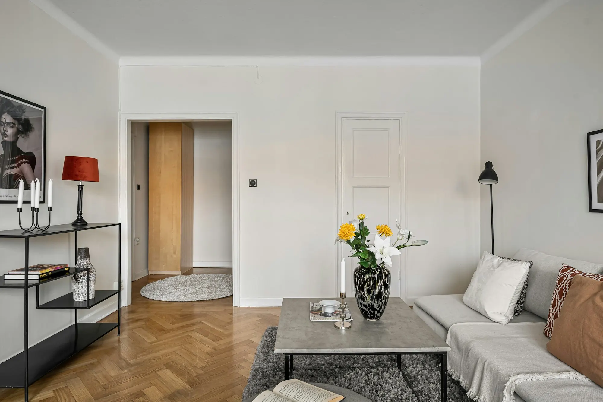 Salon sur parquet à bâtons rompus : canapé clair, table basse grise, console noire, ouverture sur l’entrée.