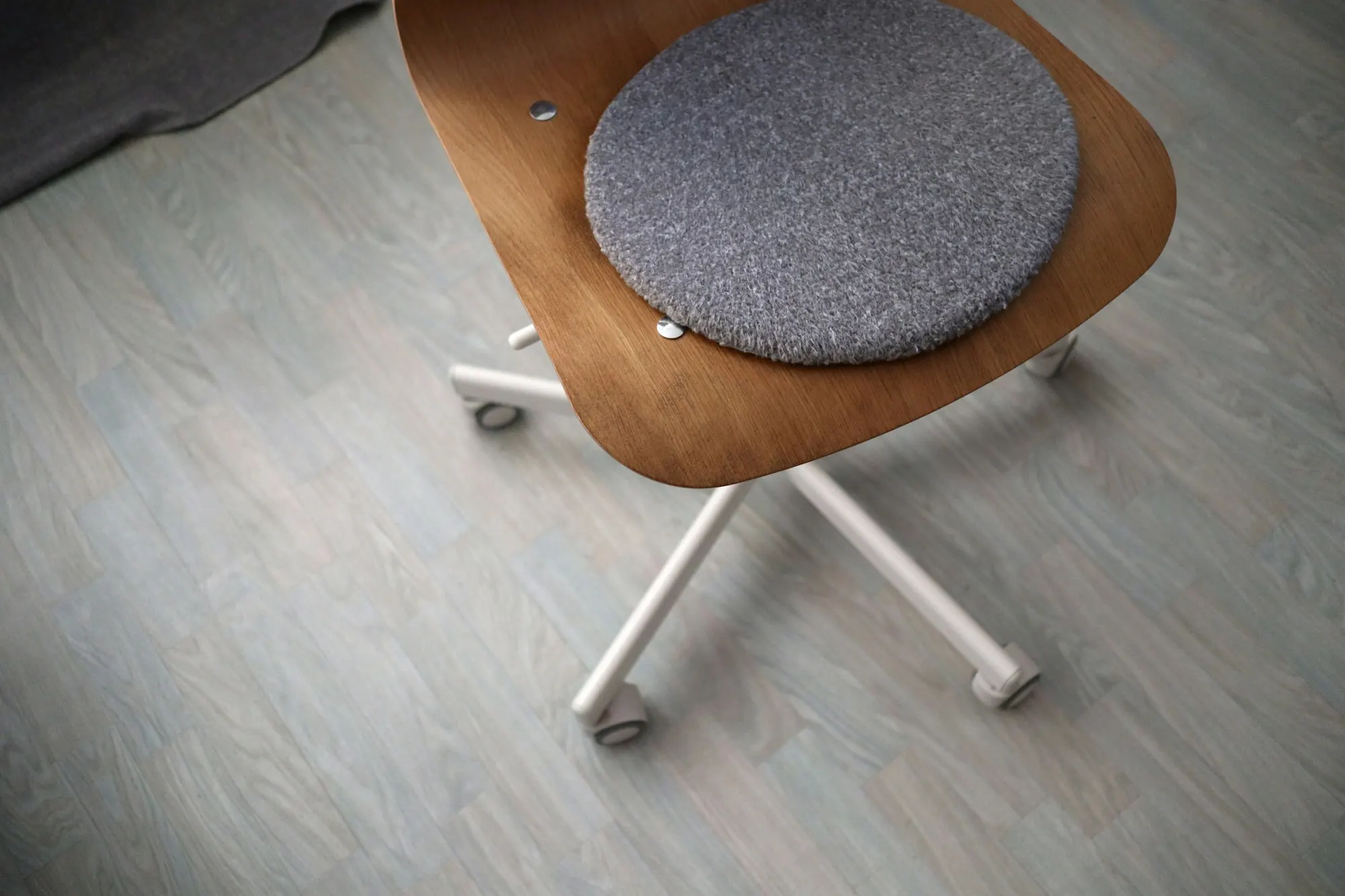 Sol à lames d’aspect bois gris clair vu de haut, chaise en bois cintré à galette de feutre gris.
